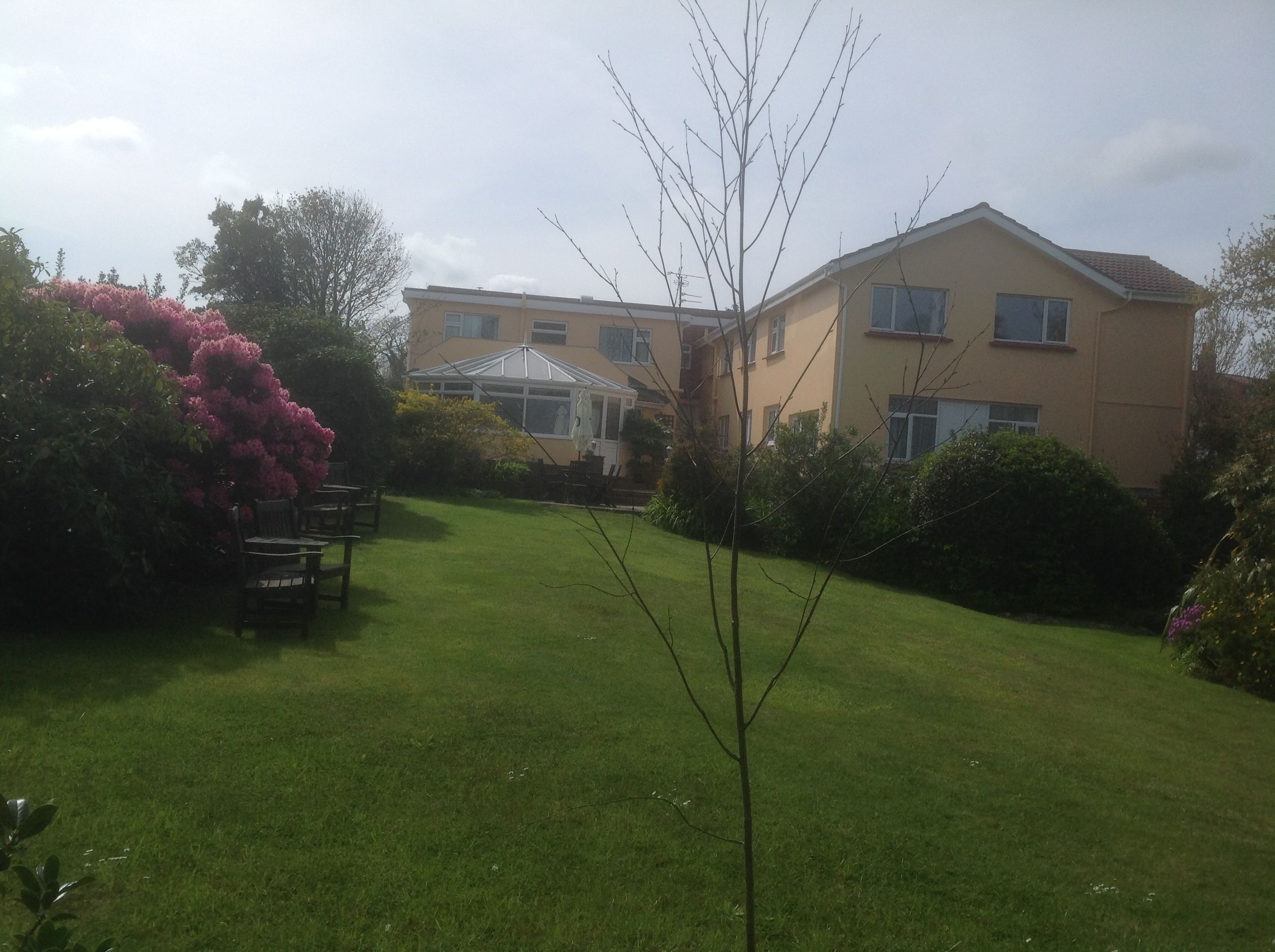 A residential building with a conservatory, a well-maintained lawn, and surrounding greenery.