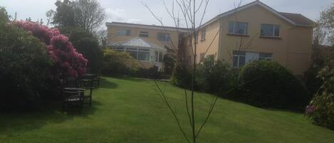 A residential building with a conservatory, a well-maintained lawn, and surrounding greenery.