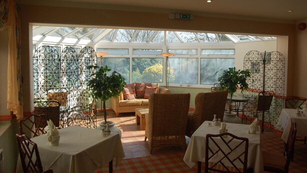 A dining area with tables and chairs, a sofa, and a view through a glass enclosure to the outdoors. - La Michele (St. Martins)