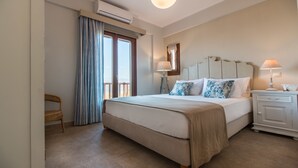 Une chambre à coucher avec un grand lit, une table de chevet, une lampe, une chaise et une fenêtre avec des rideaux.