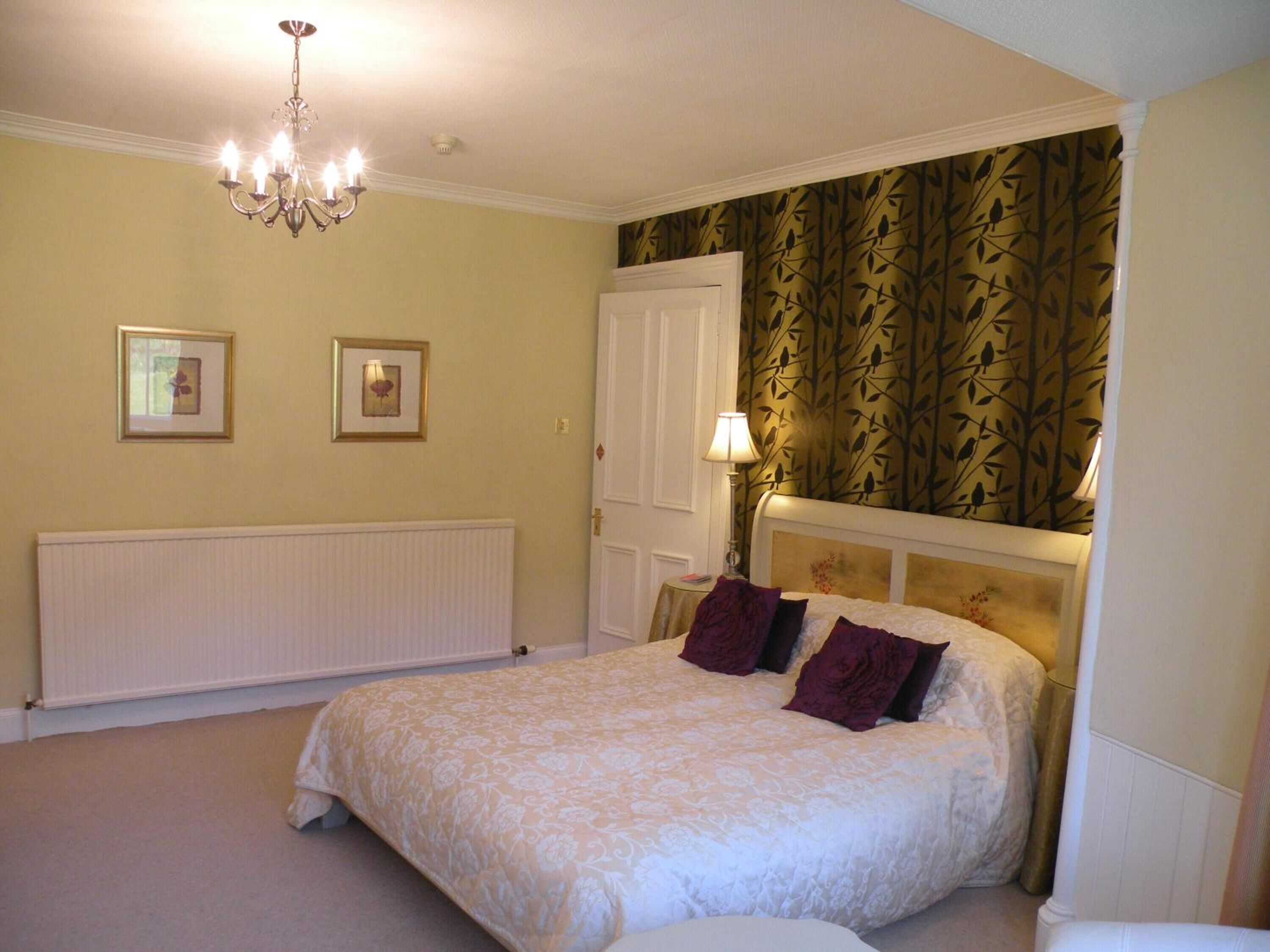 A bedroom with a large bed, a radiator, a chandelier, and two framed pictures on the wall.