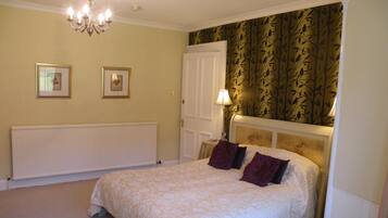 A bedroom with a large bed, a radiator, a chandelier, and two framed pictures on the wall.