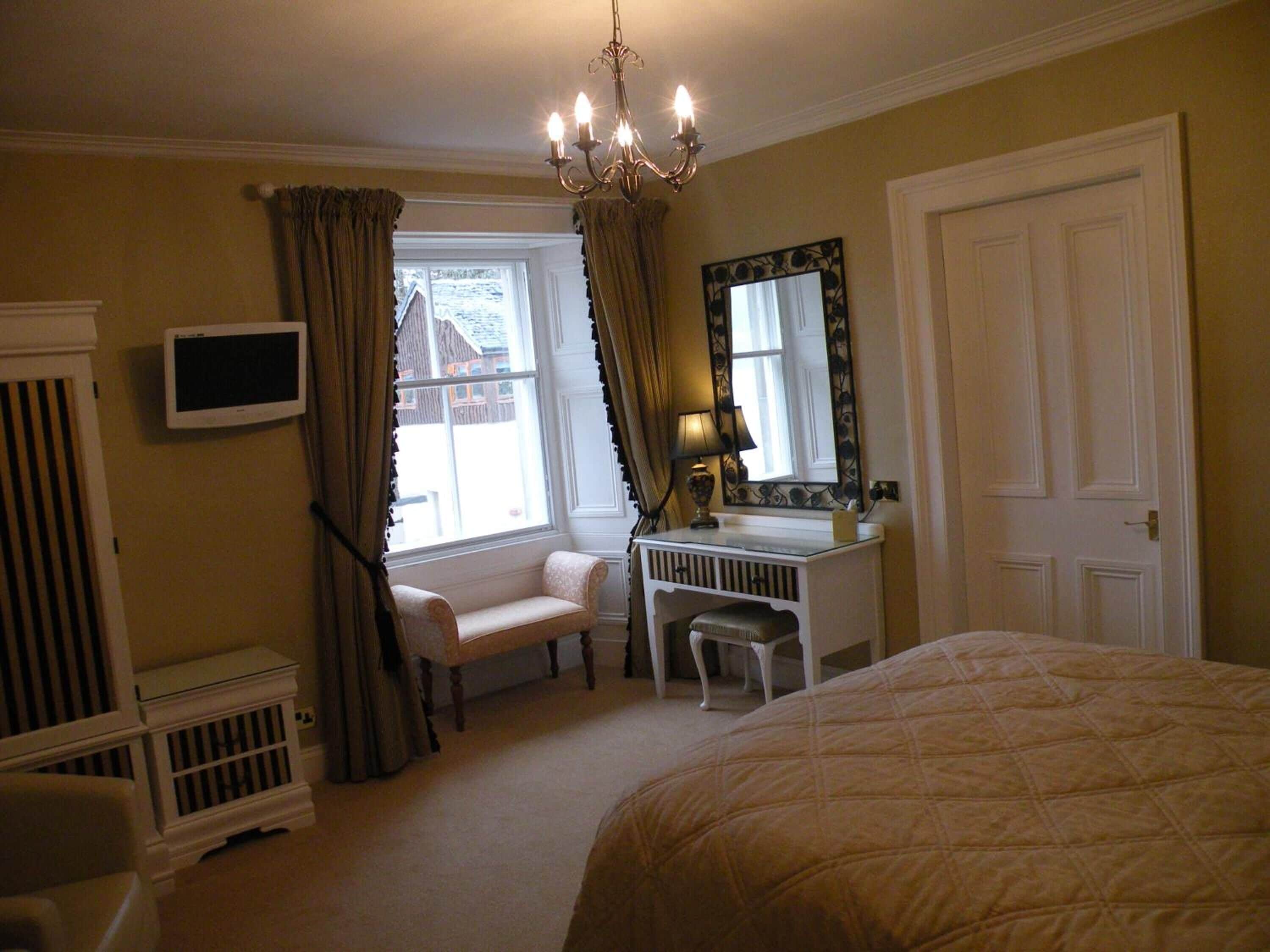 A bedroom with a bed, a desk, a chair, a television, and a window with curtains.
