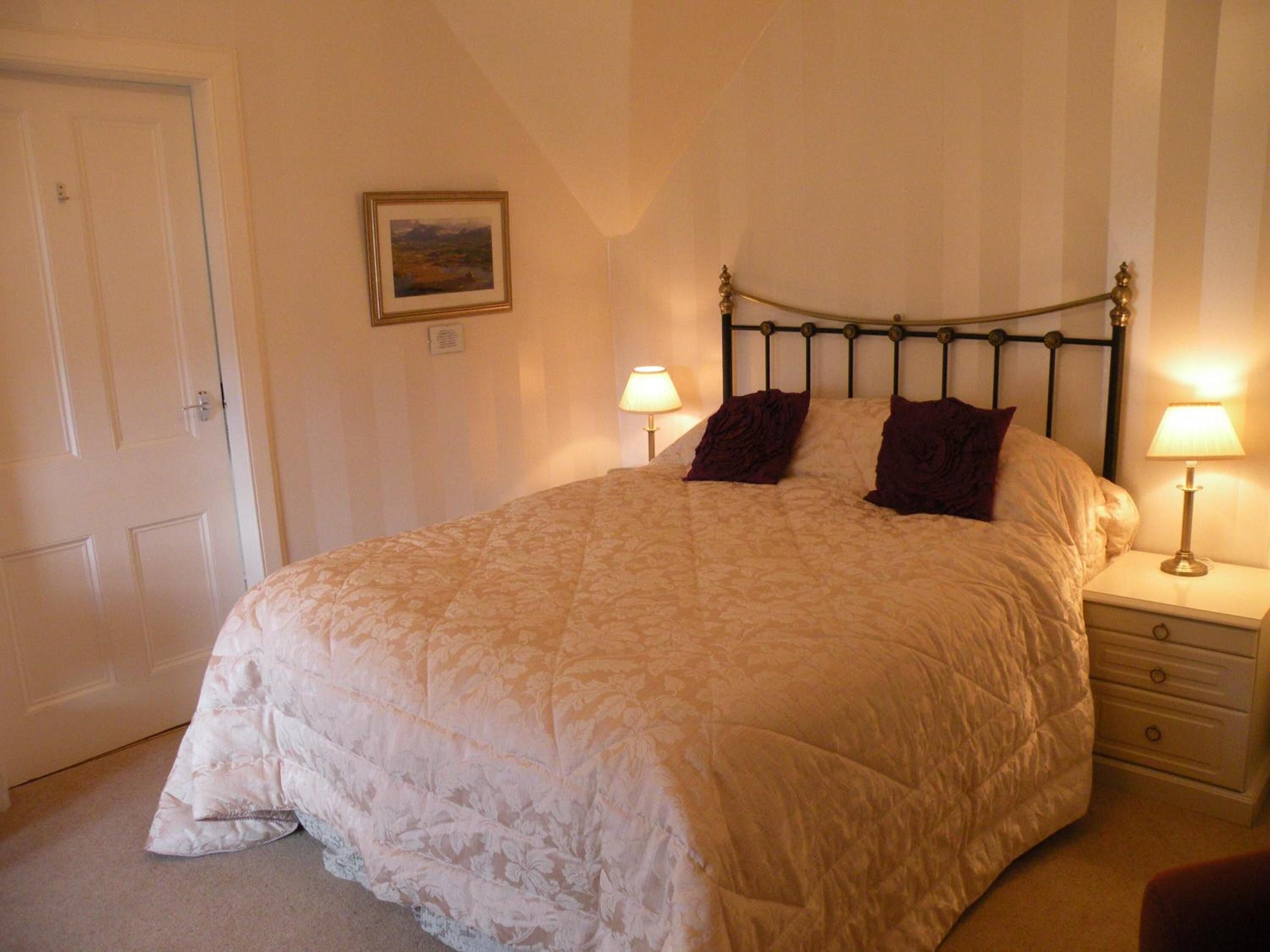 A neatly made bed with a quilted cover, two bedside lamps, a nightstand with a drawer, and a framed picture on the wall.