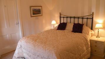 A neatly made bed with a quilted cover, two bedside lamps, a nightstand with a drawer, and a framed picture on the wall.