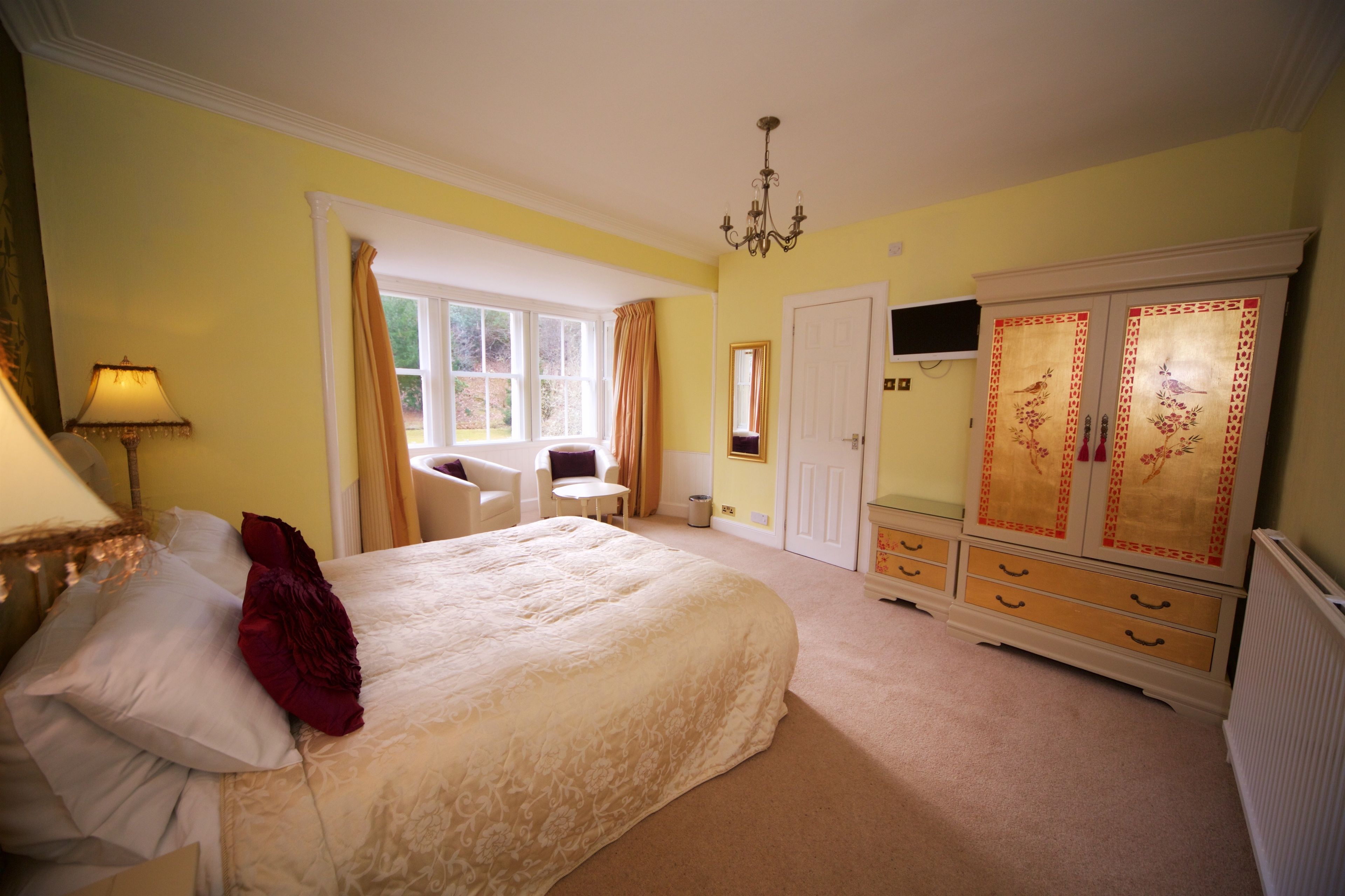 A bedroom with a bed, a desk, a chair, a wardrobe, and a television.