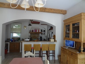 A dining area with a table, chairs, and a television on a cabinet. - L'Ancien Moulin a Huile (Tuchan)