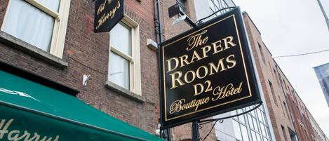 En skylt för ”The Draper Rooms Boutique Hotel” med ett grönt solskydd som visar texten ”Harrys” och en Heineken-logotyp.