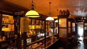 A bar with shelves of bottles and glasses, a Guinness sign, and a sign about COVID-19. - Draper Rooms (Dublin)