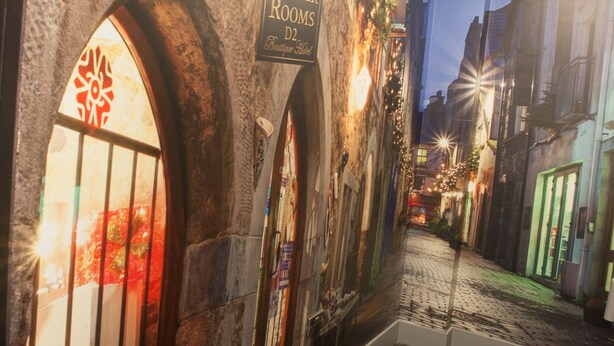 A hallway with a mural of a street scene, a sign for 'The Draper Rooms Boutique Hotel', and a security camera on the ceiling. - Draper Rooms (Dublin)