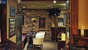 A cozy library with a brick wall, a fireplace, and a leather armchair. - Draper Rooms (Dublin)