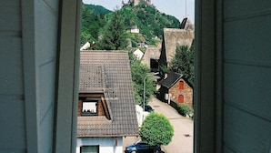 A view from a window with a triangular frame, overlooking a town with buildings, a hill, and a castle in the distance. - Haus Erholung (Cochem)
