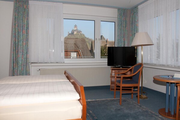 Habitación de hotel con cama, escritorio con silla, televisión y vista a un castillo a través de la ventana.