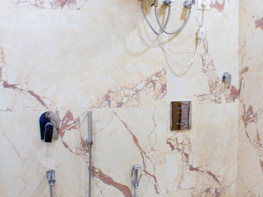 Un bagno con parete in marmo, WC bianco e box doccia sospeso.