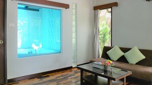 A modern living room with a large window, a sofa with cushions, a coffee table, and an air conditioning unit. - Samet Ville Resort (Rayong)