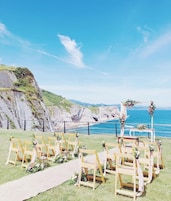 Montaje para una boda frente al mar, con sillas de madera y un arco floral.