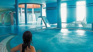 A modern indoor swimming pool with clear water, a central slide, and a seating area with chairs.