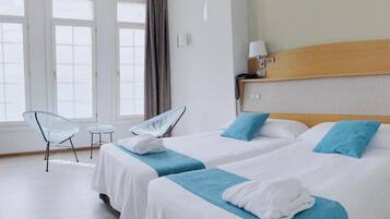 Een hotelkamer met twee bedden, een klein tafeltje, twee stoelen en een raam met gordijnen.
