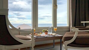 A room with a view of the sea, a dining table with breakfast items, and two chairs.