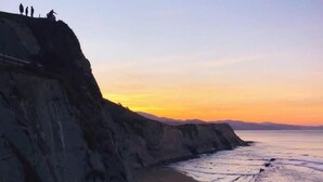 A coastal landscape with a cliff and beach at sunset.