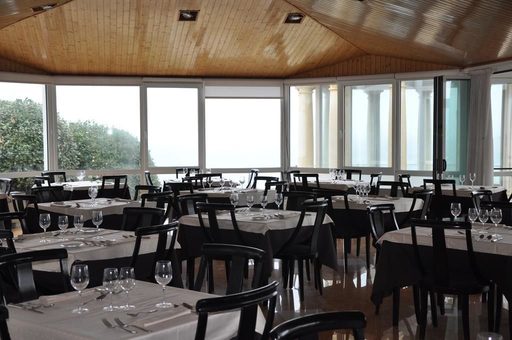 A restaurant with multiple tables and chairs, large windows, and a wooden ceiling.