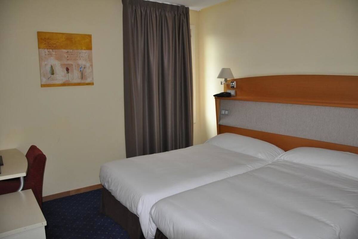 Une chambre d’hôtel avec un lit, un bureau, une chaise, une lampe et un tableau au mur.