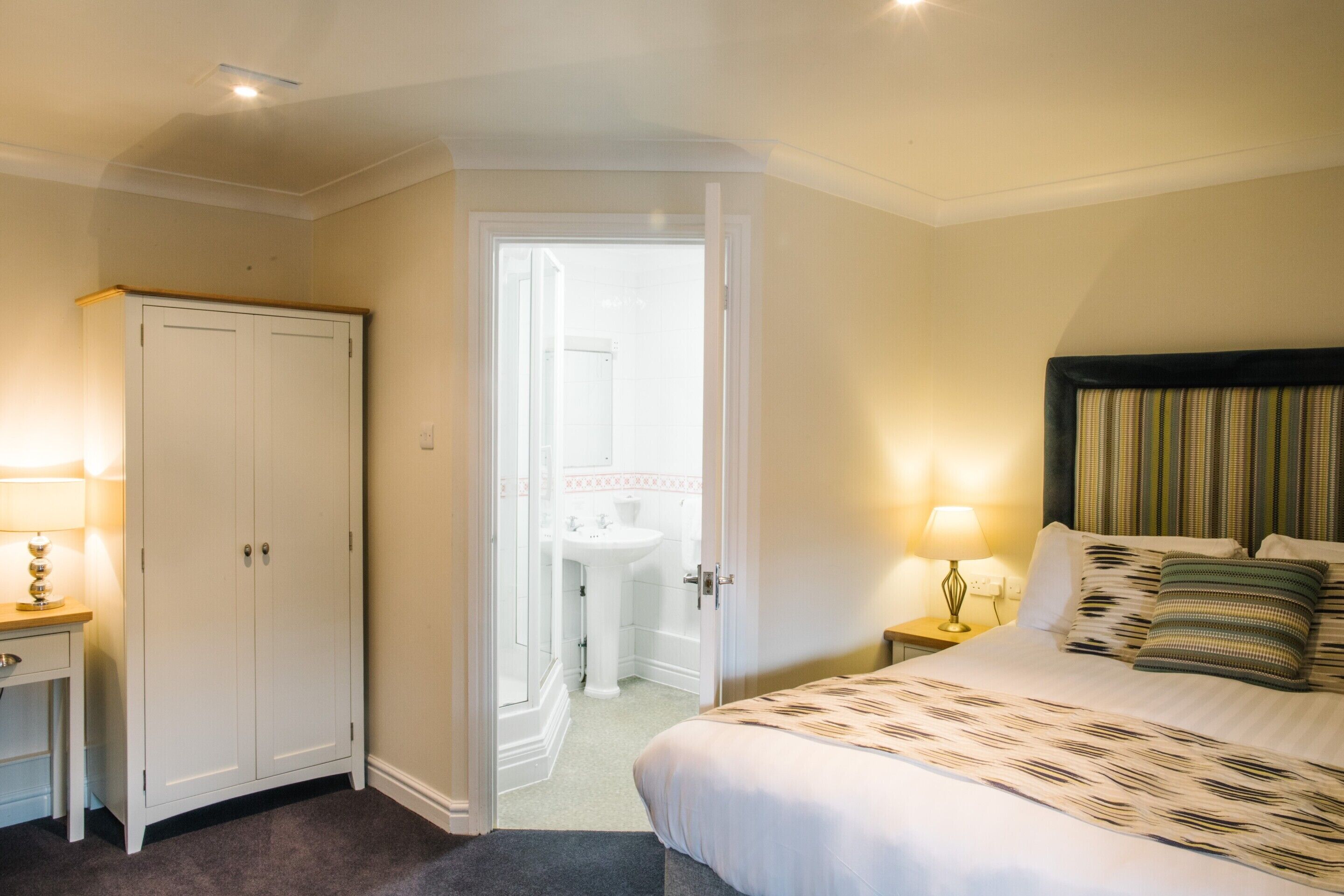 A bedroom with a bed, bedside tables, a wardrobe, and a bathroom visible through an open door.