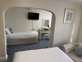 A bedroom with a bed, a desk, a chair, a television, and a framed picture on the wall.
