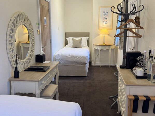 A hotel room with a bed, a desk with a mirror, a dresser, a lamp, a coat rack, and a coffee machine. - The Old Fourpenny Shop Hotel (Warwick)