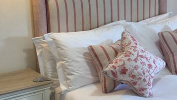 Una cama bien hecha con cabecera a rayas, ropa de cama blanca y almohadas estampadas con motivos florales.