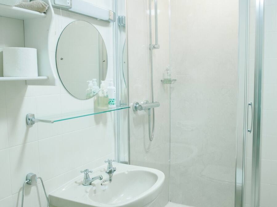 A modern bathroom with a glass shower enclosure, a pedestal sink, and a round mirror.