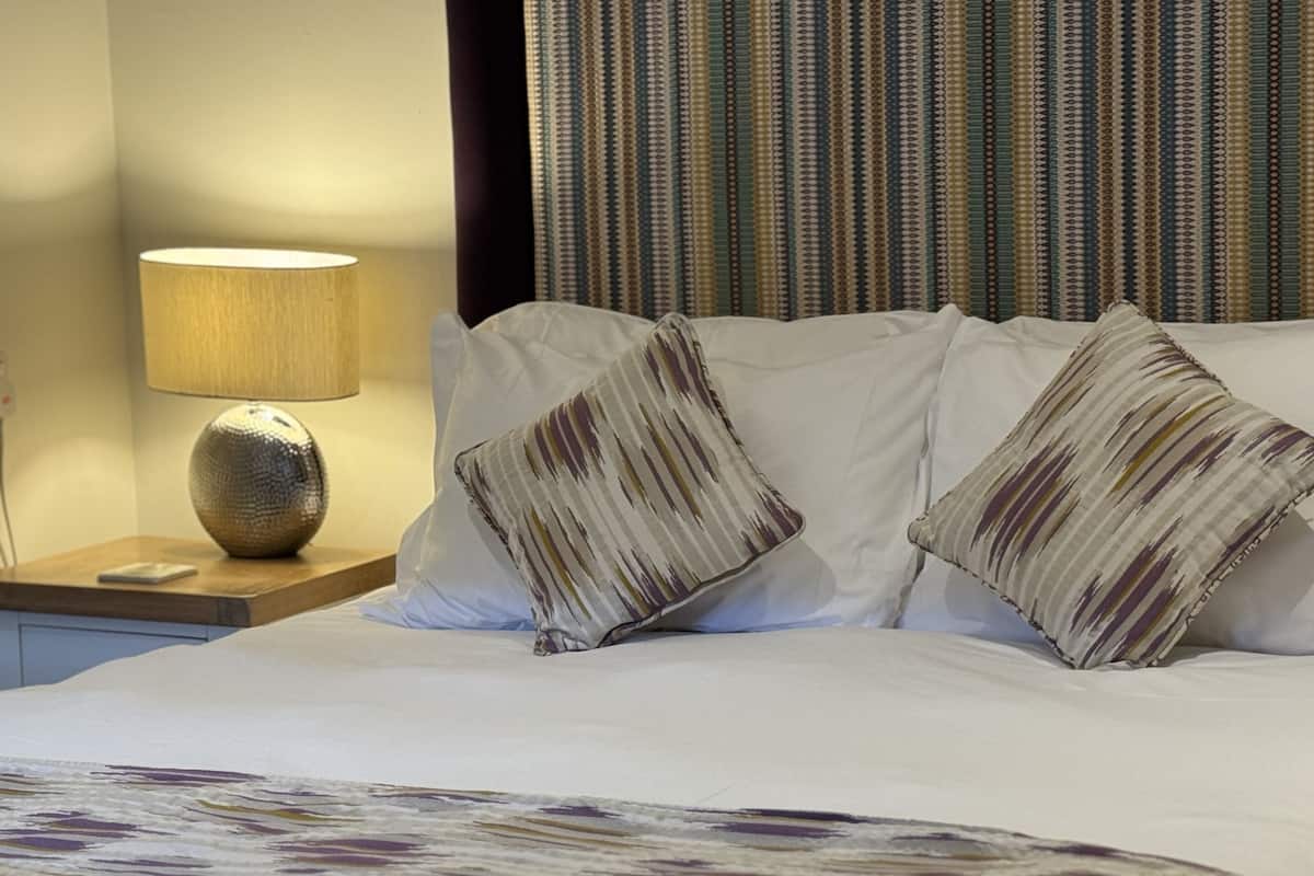 A neatly made bed with white bedding and striped pillows, a bedside lamp, and a striped curtain in the background.