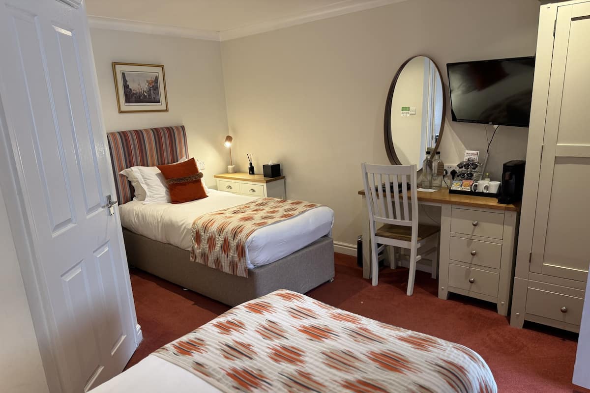 A bedroom with a bed, bedside table, chair, desk, mirror, and wardrobe.