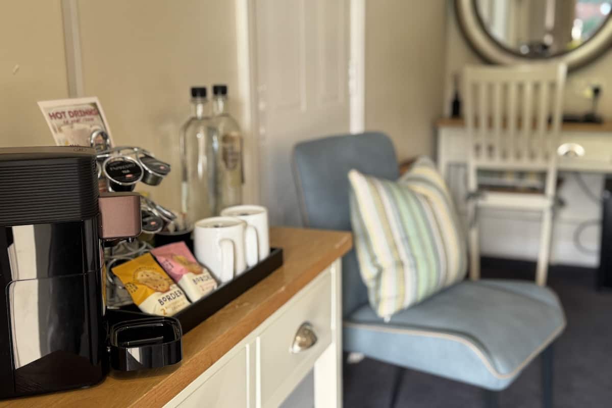 A kitchenette with a coffee maker, a microwave, and a bottle of water. There is a chair with a striped cushion and a mirror on the wall.