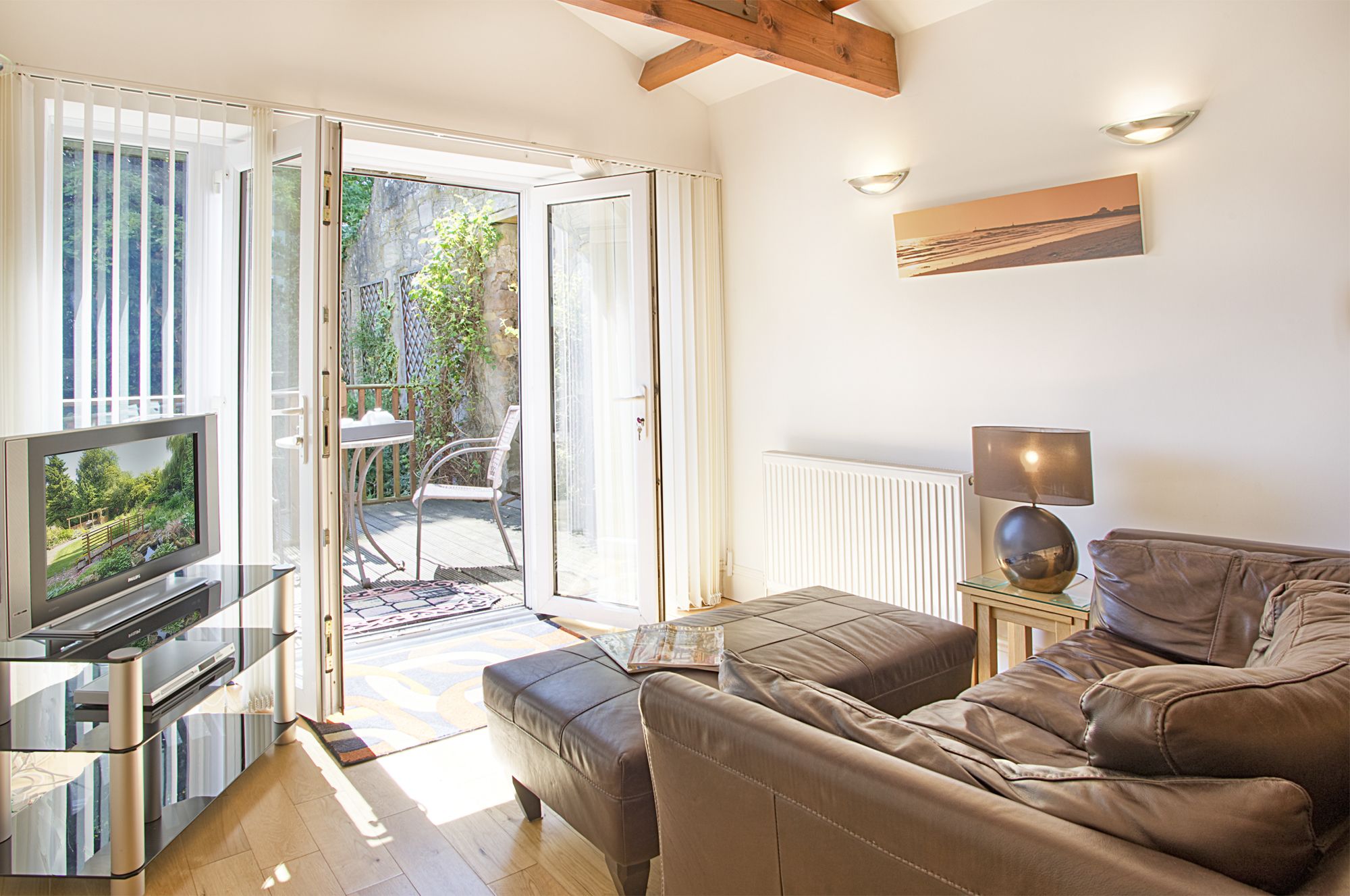 A modern living room with a sofa, a TV, a lamp, and a view of a garden through a glass door.