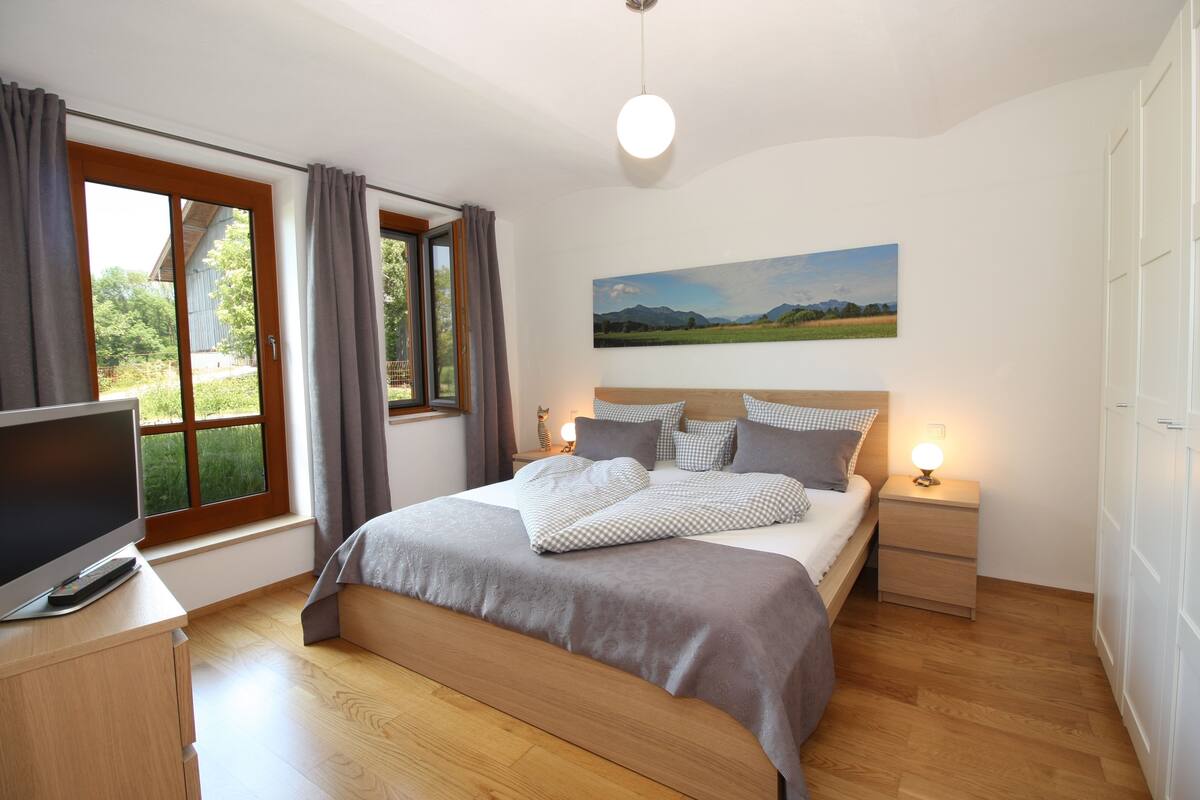 A bedroom with a bed, a TV, a bedside table, a lamp, and a window with curtains.