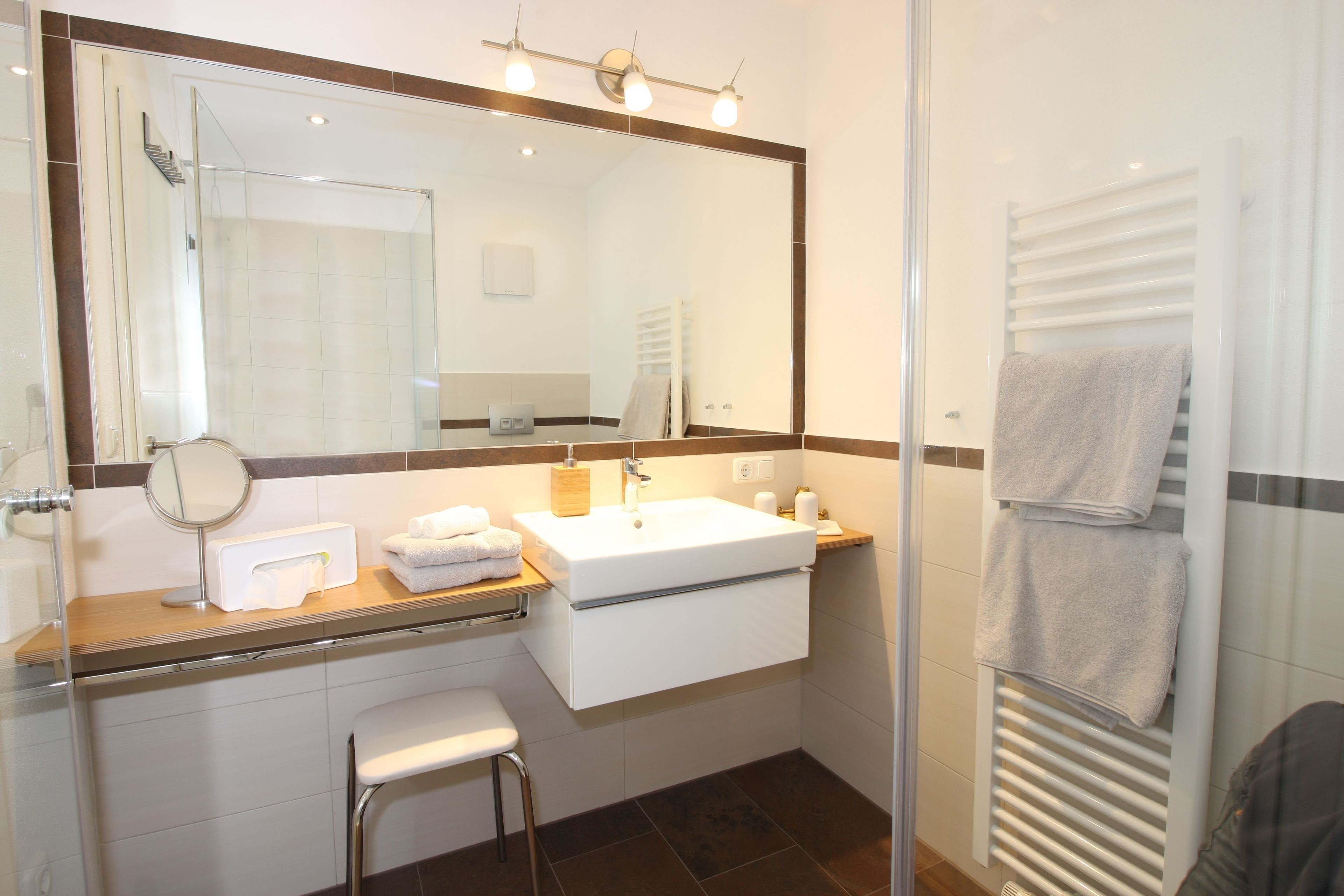 A modern bathroom with a glass shower enclosure, a large mirror, a white sink, and a towel rack.