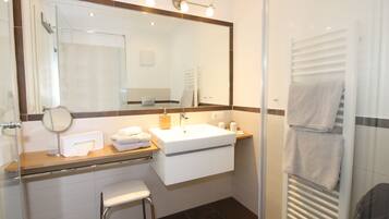 A modern bathroom with a glass shower enclosure, a large mirror, a white sink, and a towel rack.