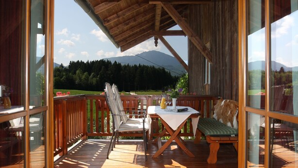 A wooden deck with a table and chairs, overlooking a mountainous landscape. - Beim Bicher (Grabenstätt)