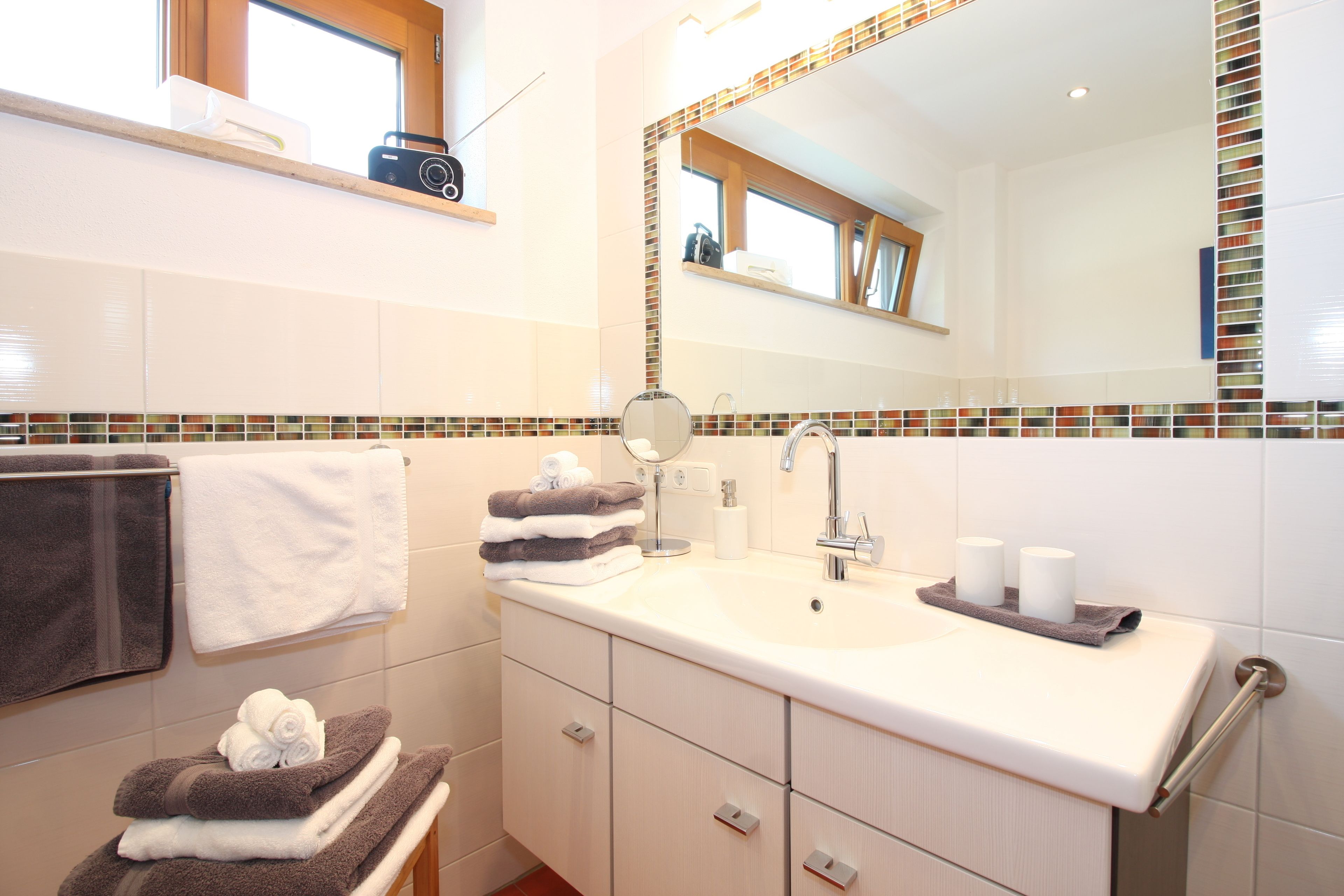 Un baño con lavamanos blanco, un espejo y un perchero con toallas.
