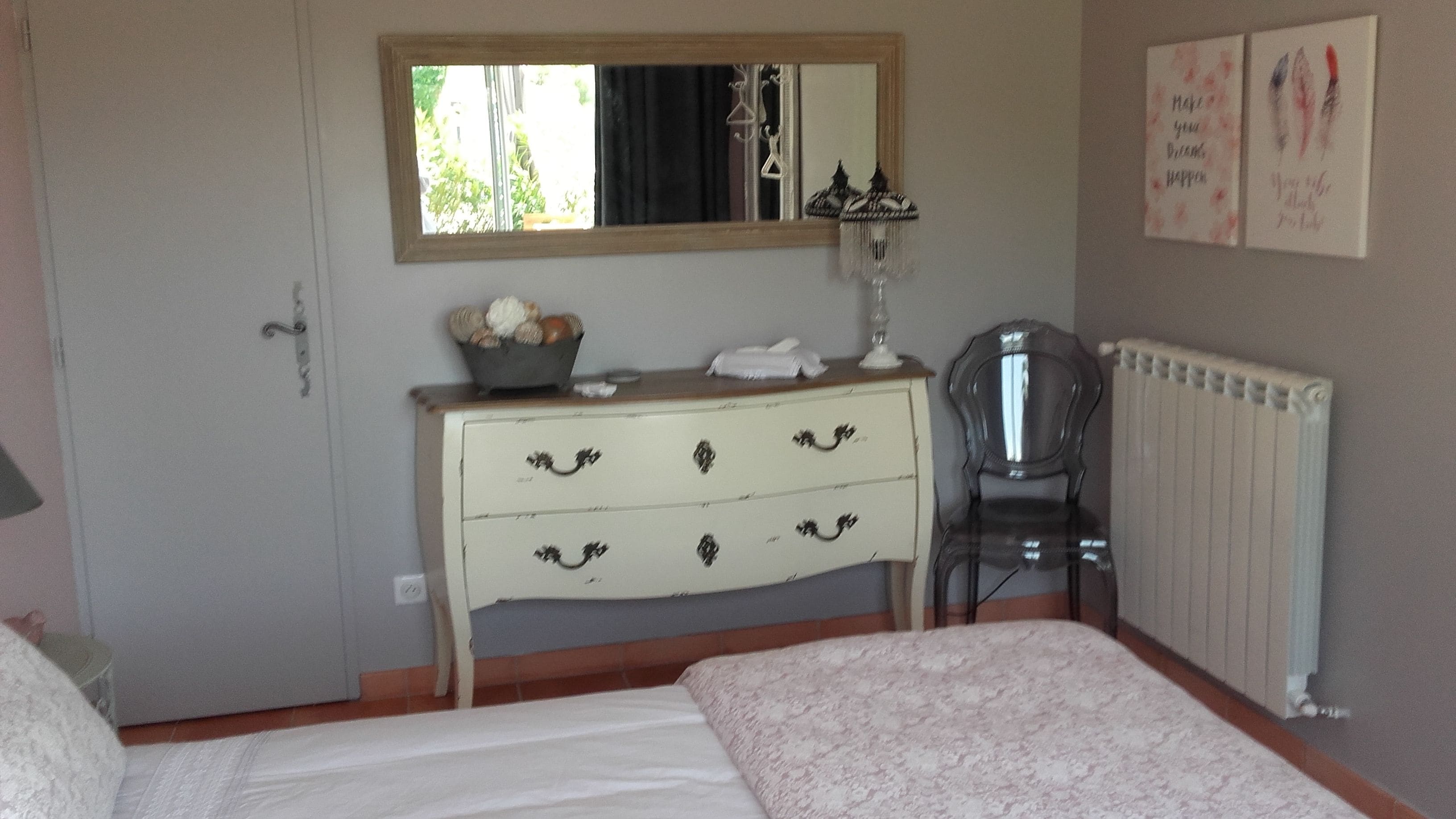 Un dormitorio con cama, cómoda con cajones, silla, radiador y decoración en la pared.