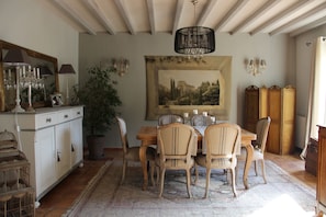 Uma sala de jantar com mesa e cadeiras de madeira, um candelabro e uma pintura de paisagem grande na parede.