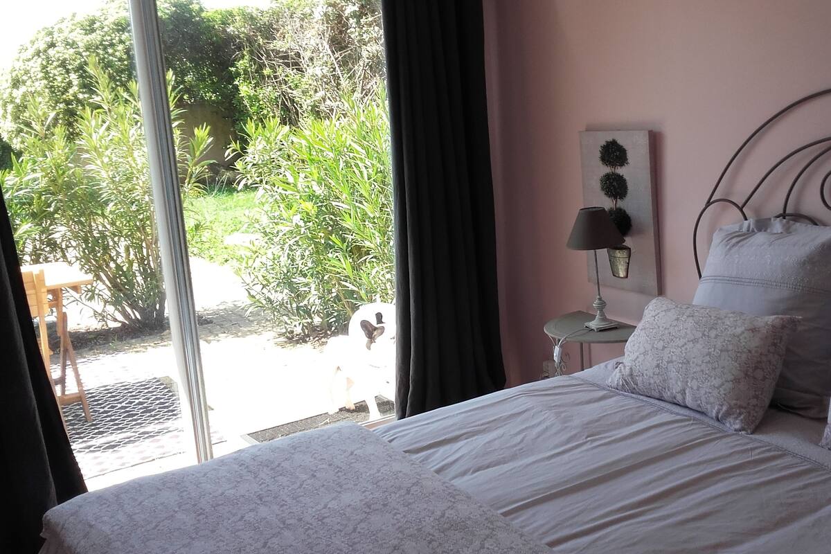 Une chambre à coucher avec un lit, une table de chevet, une lampe et une vue sur la verdure.