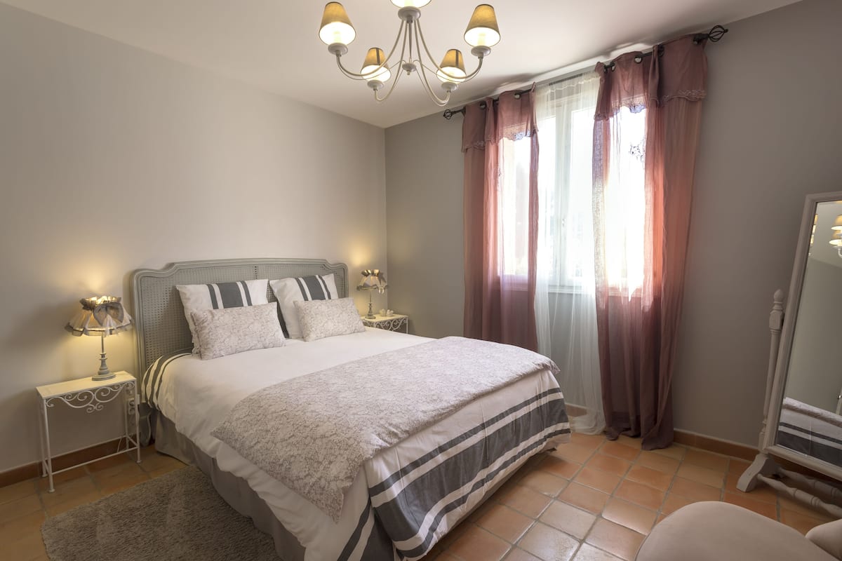 Une chambre à coucher avec un lit, des tables de chevet, un miroir et un lustre.