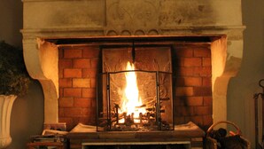 A fireplace with a fire, a mantel with decorative items, and a brick wall. - La Bastide du Bouchou (Six-Fours-les-Plages)