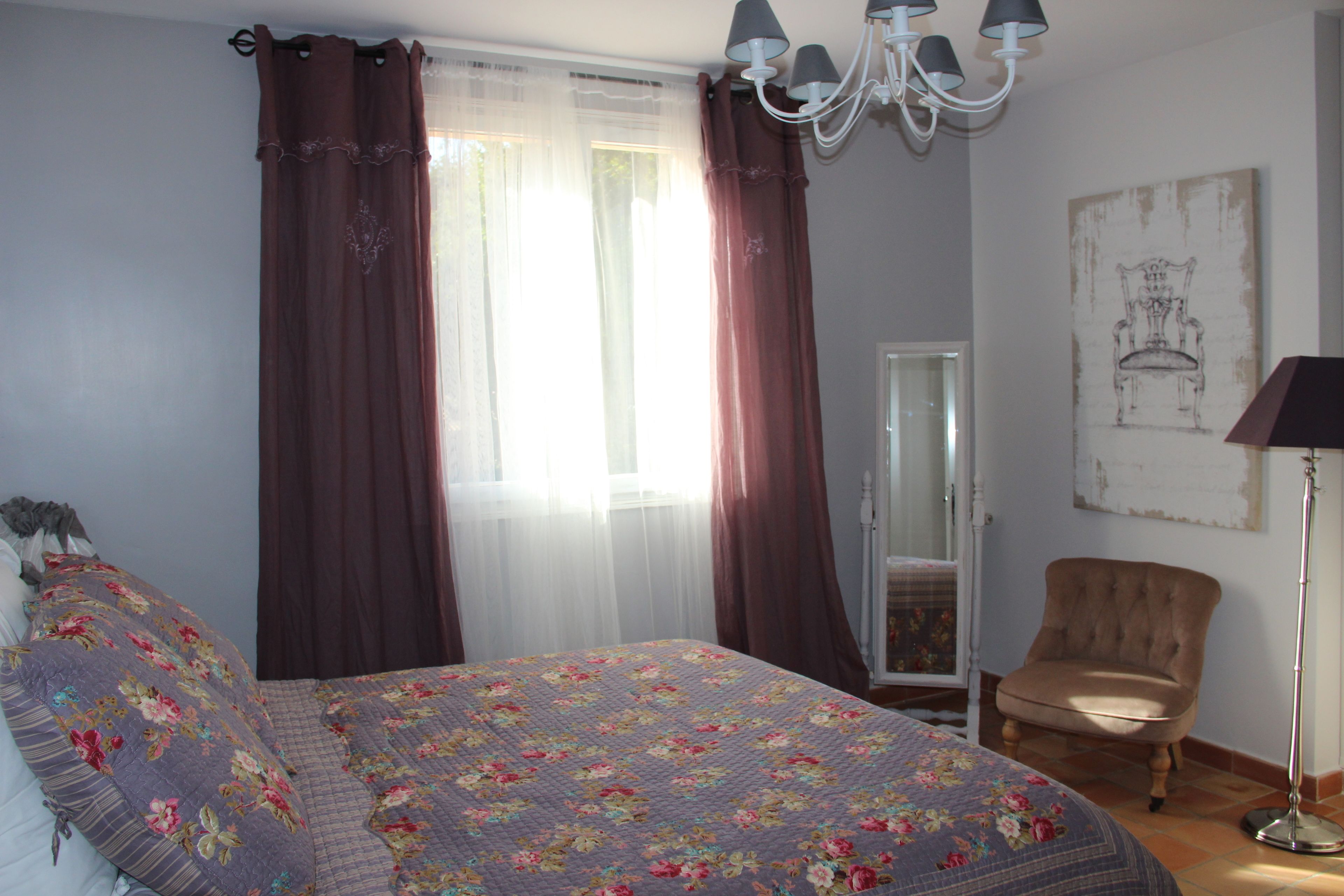 Un dormitorio con cama, una silla, una lámpara de pie, un espejo y un cuadro en la pared.
