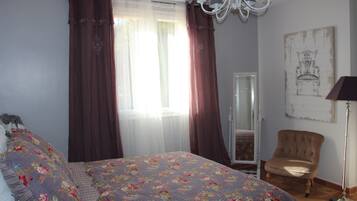 Un dormitorio con cama, una silla, una lámpara de pie, un espejo y un cuadro en la pared.