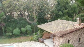 A rustic house with a tiled roof, a stone pool, and lush greenery.