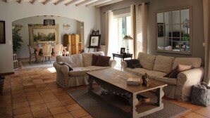 A spacious living room with a large wooden coffee table, two beige sofas, and a dining area with a wooden table and chairs. - La Bastide du Bouchou (Six-Fours-les-Plages)