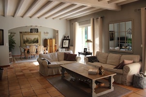 Un salon spacieux avec une grande table basse en bois, deux canapés beige et un coin repas comprenant une table et des chaises en bois.